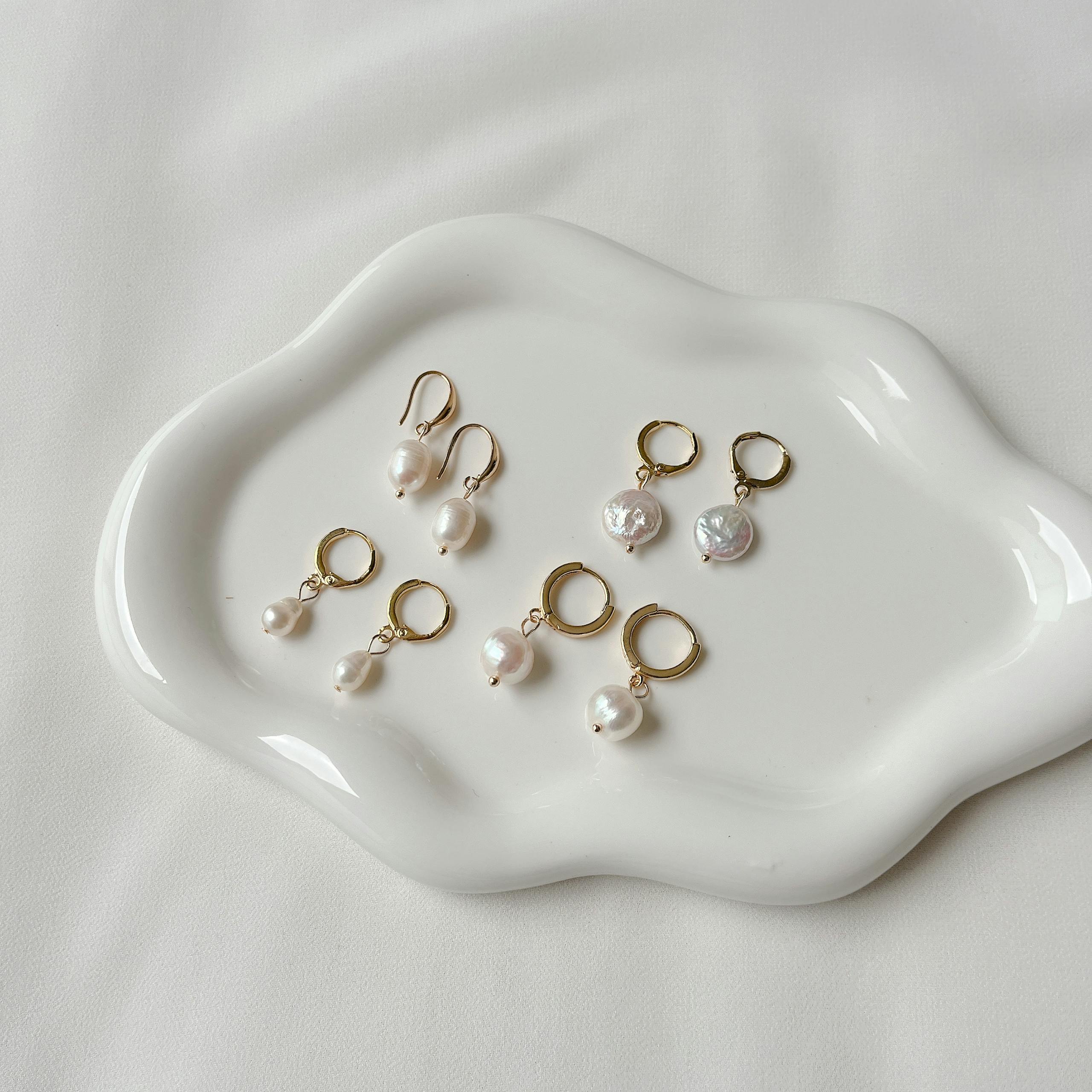 A collection of elegant pearl earrings displayed on a white ceramic tray, offering a minimalist style.